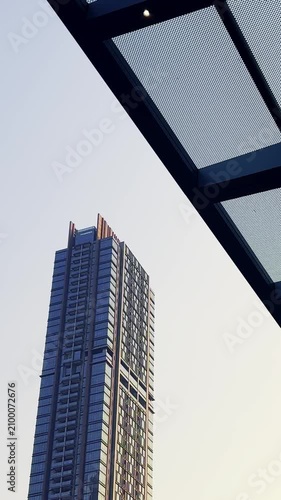 Tall modern skyscraper rises beside a geometric steel canopy against a pale urban sky.