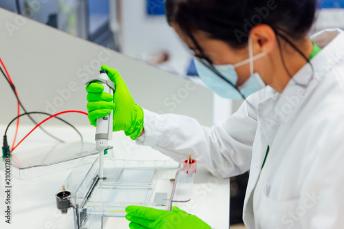 Female medical expert using pipette on electrophoresis apparatus while testing in lab