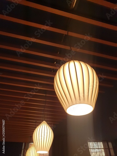 Warm pendant lamps hang from a slatted wooden ceiling casting soft ambient glow and creating a cozy, modern interior atmosphere ideal for restaurants, cafes, hotels, and contemporary living spaces.