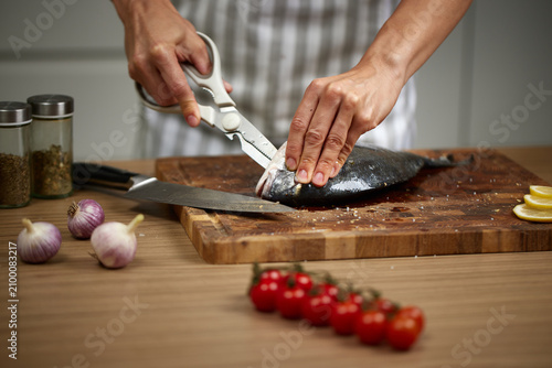 Chef preparing fresh sea bream using kitchen shears