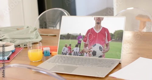 Male soccer player holding ball on laptop at home table, focus marker appearing centering face