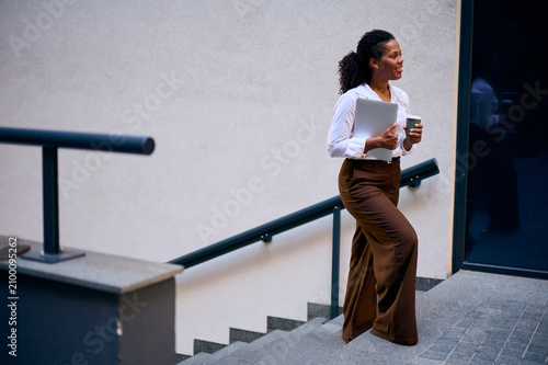 Confident African American Business Woman Walking Up Stairs With Laptop And Coffee Cup