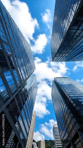Modern glass skyscrapers rise into a bright blue sky