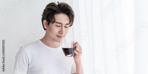 Portrait of young handsome asian man hands holding coffee glass cup morning spring time in white bedroom. Happy cheerful relaxing in summer. Korean male guy wakeup, university asia lifestyle concept