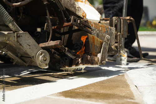 Workers using a professional road marking machine to apply hot thermoplastic paint on a concrete surface for traffic line striping.