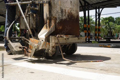 Workers using a professional road marking machine to apply hot thermoplastic paint on a concrete surface for traffic line striping.