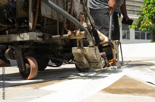 Workers using a professional road marking machine to apply hot thermoplastic paint on a concrete surface for traffic line striping.