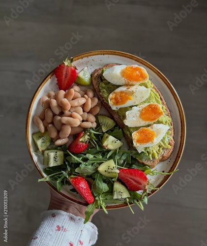 Healthy breakfast bowl with sunny side eggs, fresh vegetables, white beans and crisp greens served on a rustic plate. A colorful, nutritious meal perfect for healthy eating, fitness, diet and lifestyl