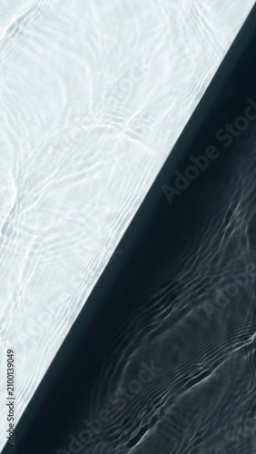 A clear water surface with a sharp geometric shadow line across ripples, vertical 9:16 top-down view.