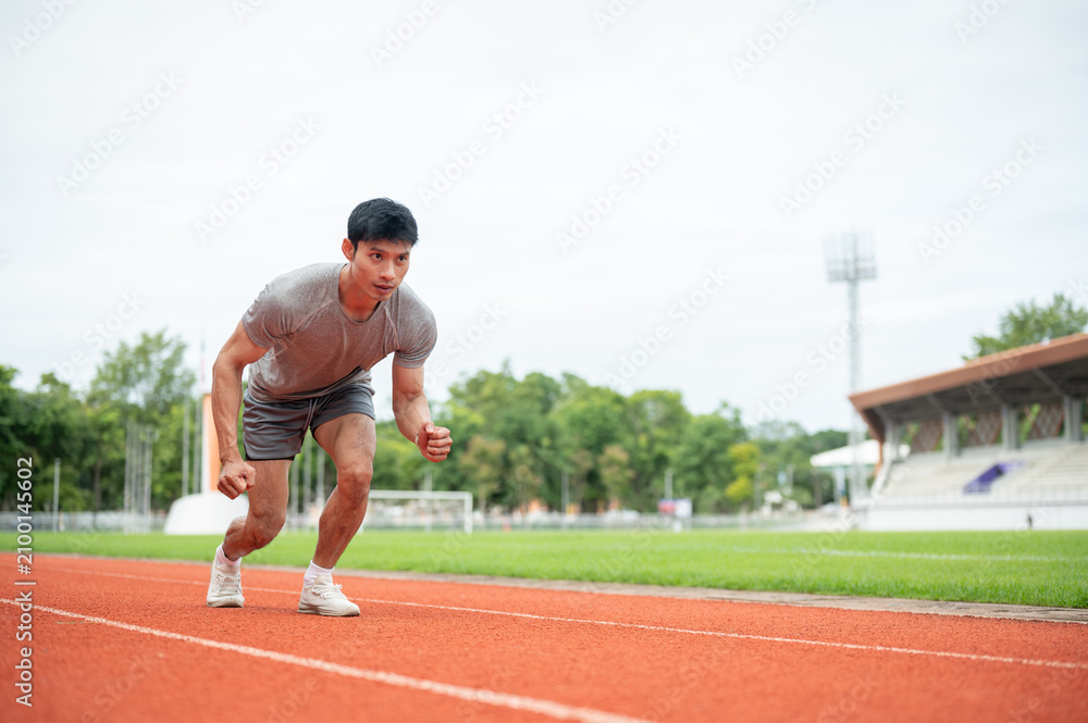 Fototapeta premium Asian athletic man launching from start line on running track in sports stadium.