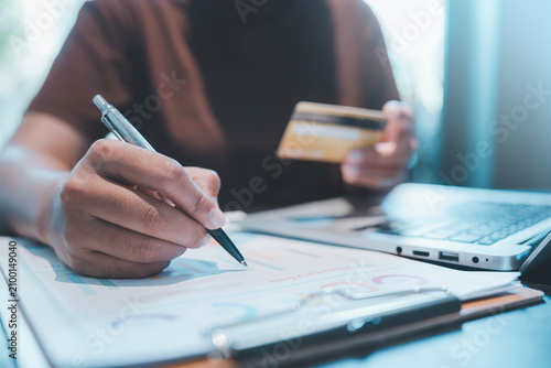 Online payment and financial accounting concept person holding credit card writing on data chart document with pen for analyzing business budget expense tracking and internet banking transaction