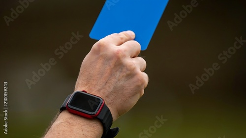 A hand wearing a smartwatch holds up a blue card in a sporting event.