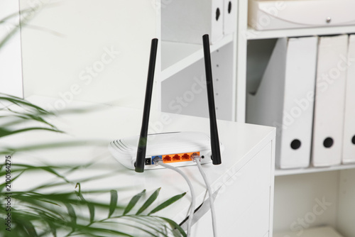 Fotografie White wireless router with two antennas and connected ethernet cables on a desk