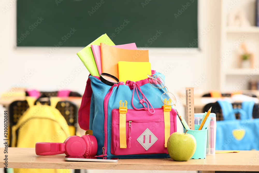 Obraz premium Colorful school backpack filled with books and supplies on a classroom desk, back to school
