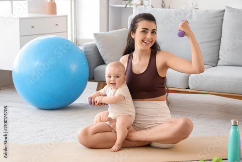 Sporty young woman with her little baby and dumbbells training at home