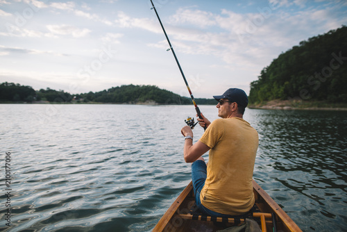 Rear side view of a man fishing from a wooden canoe 