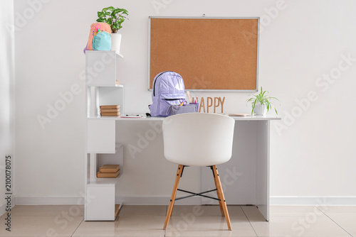 Workspace with school supplies, pinboard and backpack near white wall