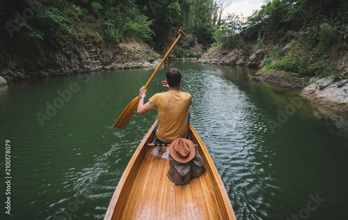 Rear view of male adventurer canoeing through forest lake