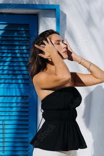 Woman touching face beside blue shuttered wall outdoors