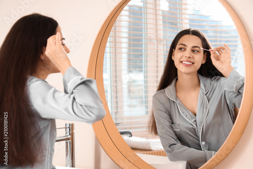 Beautiful young happy woman with cotton bud removing makeup near mirror at home