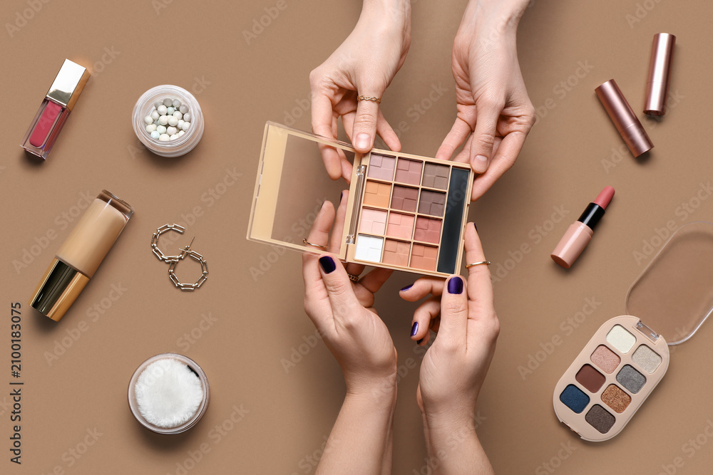 Obraz premium Female hands with different decorative cosmetics and earrings on brown background