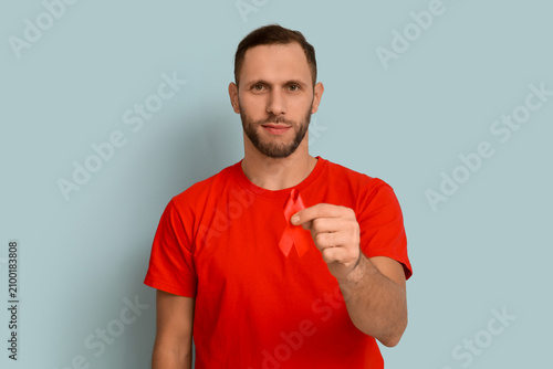 Young man with red ribbon on blue background. AID awareness concept