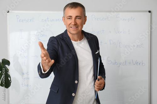 Male teacher with clipboard conducting English grammar lesson in classroom