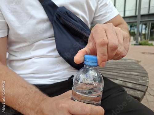 Man opening a plastic bottle of pure drinking water outdoors. close up view, drinking water, healthy lifestyle, plastic bottle.