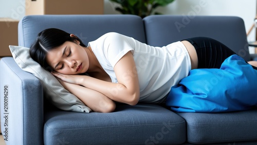 Exhausted Rest: A young woman sleeps deeply on a sofa, clutching a blue pillow, appearing tired and seeking comfort. Her relaxed posture suggests a need for respite.