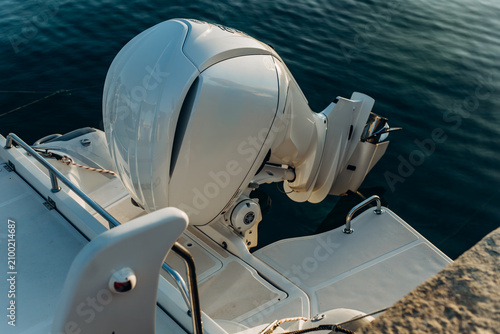 White outboard engine tilted up on the stern of a boat moored beside dark green water. Marine engine technology and boat maintenance for the watercraft service and rental industry