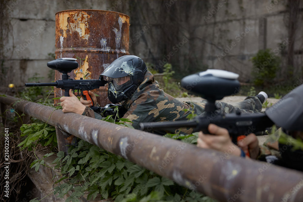 Fototapeta premium A soldier aims a gun while leaning on a pipe, lying on the ground