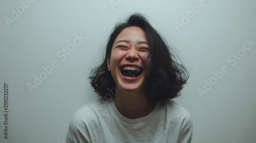 Young Asian woman laughing loudly with eyes closed