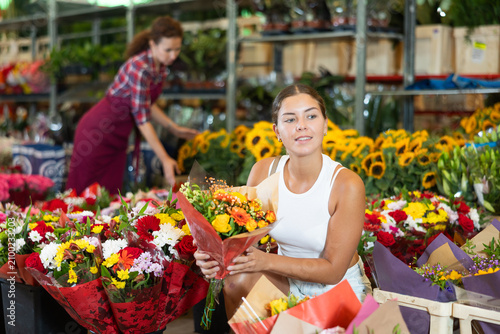 Bild auf Leinwand Young woman buyer examines bouquets of fresh flowers, chooses floral arrangement, gift
