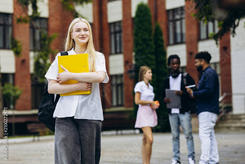 Konstfotografi Young blonde student embracing education, holding a yellow folder and a backpack