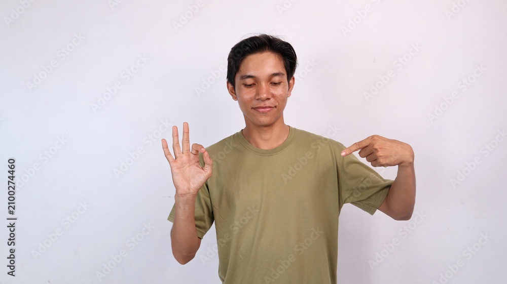 Fototapeta premium Asian young man smiling gestures pointing and looking at the middle side of the copy space and hands okay yes