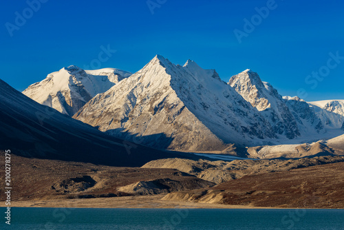 Dark mountain slopes meet a bay and lead to snowbound peaks under a blue sky in Greenland