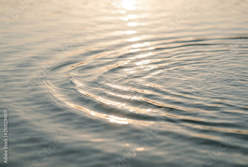 Gentle ripples on the water surface from a light splash, reflecting the warm golden glow of the sunset and creating calm atmosphere
