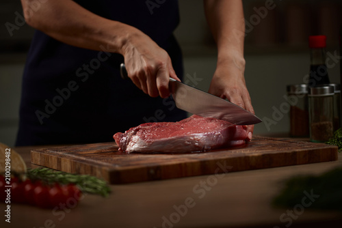 Fotografie Chef slicing raw red meat on cutting board