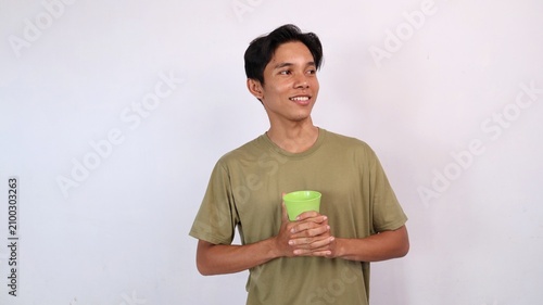 Canvastavla smiling young asian man holding cup and glancing sideways