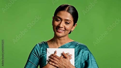 Joyful Woman in Teal Traditional Outfit Holding White Envelope Against Bright Green Background Expressing Happiness and Surprise