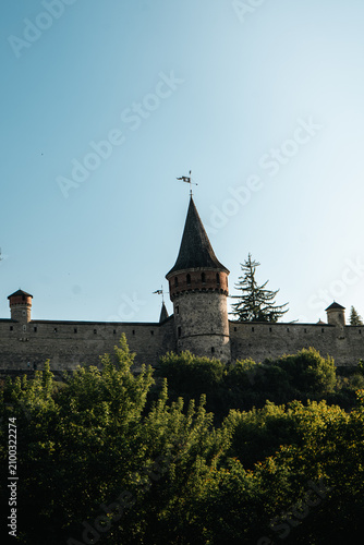 Ancient stone fortress with conical tower and flags against a clear blue sky