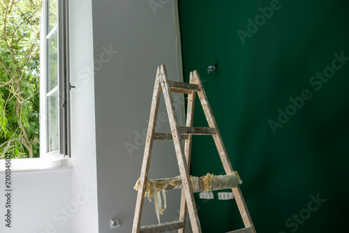 Professional painter applying deep green paint with roller on modern interior accent wall during home renovation in bright residential room with natural light,