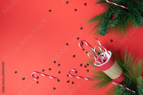 Cheerful, holiday flat lay with paper coffee takeout cup containing coffee beans and candy canes for a peppermint mocha on a bright red background.