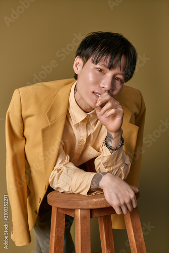 Foto Young man with a trendy outfit playfully leans on a stool, showcasing his fashionable style