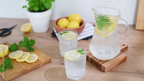 Refreshing lemonade pitcher and glasses with mint and lemon slices on a wooden surface