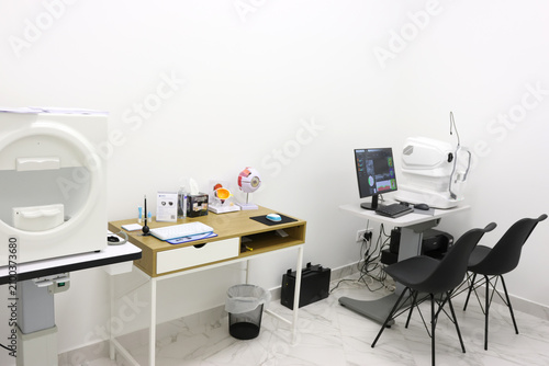 Modern ophthalmology office with diagnostic equipment, computer, eye model and doctor workstation.