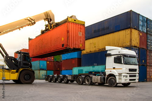 Truck while loading in logistic shipping yard with cargo container. Forklift truck handling truck. Logistic import export concept. Loading and unloading of containers in the port