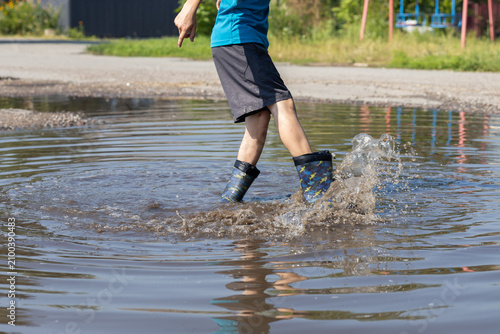cropped image of a child in rubber boots joyfully splashing in a puddle after a summer rain. The freedom of childhood happily spending summer days. Changeable weather