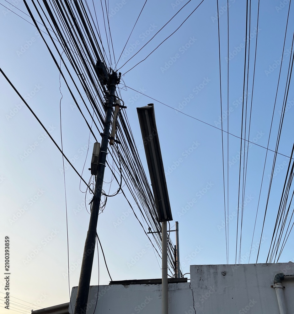 Obraz premium Utility pole with tangled power lines against a blue sky