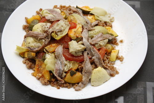 Appetizer, side salad with buckwheat, artichokes, tomatoes, zucchini, anchovies, olive oil, basil, herbs.